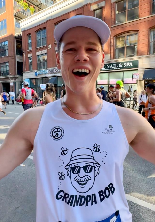 Joey mid-race at the Chicago Marathon, grinning at the camera in a white cap and a Grandpa Bob singlet